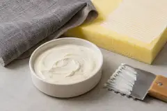 Foam and fabric layers bonded on a bench, with a spray gun and a tub of water-based adhesive