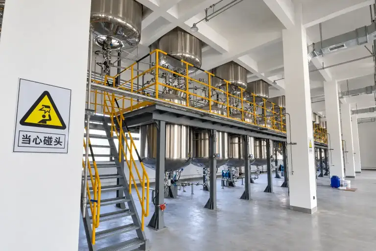 Production hall with jacketed vessels on a raised steel platform and a caution sign at the stairway