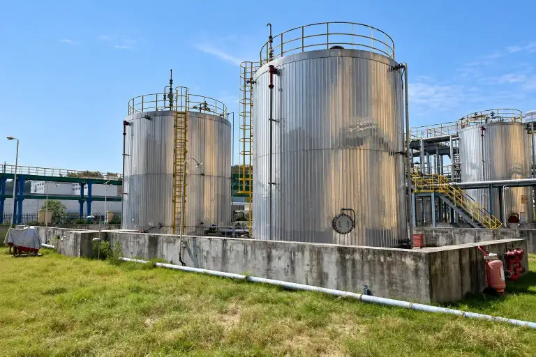 Bulk solvent storage tanks on a bunded concrete base outside the production building, with pipework running to the plant
